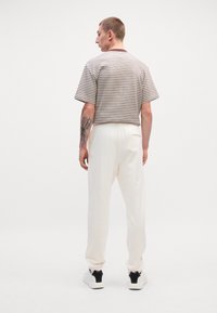 Koszulka w paski z krótkim rękawem w odcieniach beżu i brązu, w zestawieniu z kremowymi spodniami dresowymi. Posiada luźny krój i miękki materiał, noszona z czarno-białymi tenisówkami.