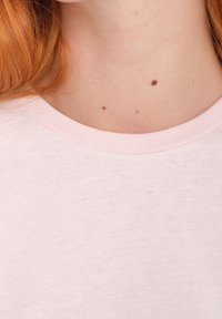 Vaaleanpunainen t-paita, jossa on pyöreä pääntie ja resorikaulus. Kangas näyttää pehmeältä ja sileältä.