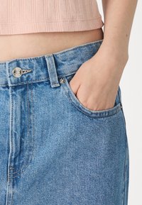 Ljusblå denimjeans med hög midja, med en framficka, kopparstyg och metallknappringning. Släta i texturen.