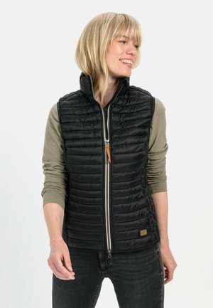 Zwarte puffer gilet met verticale gestikte textuur, hoge kraag en rits aan de voorkant. Draag het over een olijfgroene blouse met lange mouwen. Effen zwarte jeans.