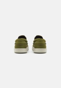Green canvas slip-on shoes with padded collar, rubber soles, and white stitching. Textured fabric and minimalistic design.