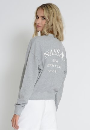 Grå sweatshirt med en afslappet pasform og lange ærmer. Har hvid trykt tekst på ryggen, der står "NASSAU IBIZA BEACH CLUB 2008."