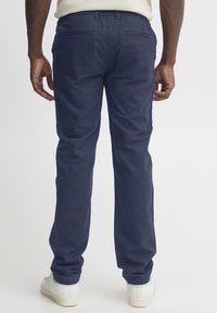 Mørkeblå, rette bukser med en glatt tekstur og baklommer, kombinert med hvite joggesko. Midjebåndet har lett elastikk for bedre passform.