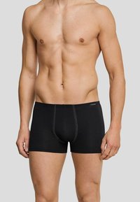 Black boxer briefs made of soft fabric, featuring white stitching, a snug fit, and a horizontal fly opening.