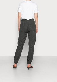Pantalon cargo en coton gris avec une ceinture élastique, deux poches arrière, jambes fuselées et bas élastiques, assorti à un t-shirt blanc uni.
