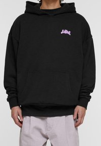 Musta huppari, jossa on etutasku, ylivertainen istuvuus ja vaaleanpunainen "Lost"-logo vasemmassa rinnassa. Valmistettu pehmeästä kankaasta, jossa on sileä pinta.