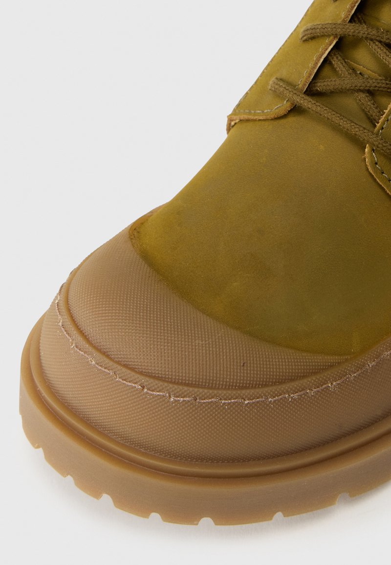 Chaussures vertes et beiges avec une tige en daim texturé et une semelle en caoutchouc. Bout rond avec des accents de couture visibles et un design légèrement surélevé.