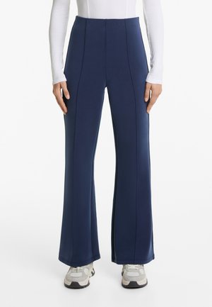 Navyfarbene Schlaghosen aus dehnbarem Stoff mit vorderen Nähten. Kombiniert mit hellen Sneakers, die einen entspannten, sportlichen Look zeigen.
