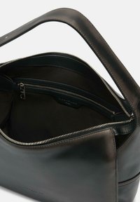 Sac à main en cuir noir avec une fermeture éclair sur le dessus, un intérieur spacieux et une poche intérieure zippée, affichant une texture lisse et une sangle robuste.