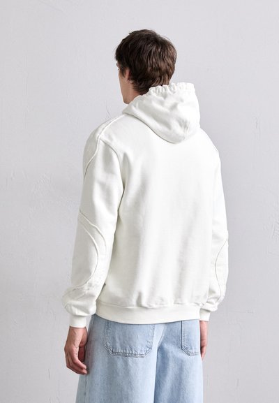 Sudadera blanca con capucha y un corte relajado, que presenta puños y dobladillo acanalados, detalles de costura sutiles y una textura de felpa suave.