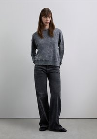 Szara bluza z efektem sprania, z okrągłym dekoltem, zestawiona z pasującymi szerokimi spodniami dżinsowymi w tym samym odcieniu szarości. Materiał wydaje się miękki, o delikatnej fakturze i subtelnym wyblakłym efekcie.