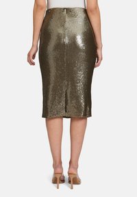 Jupe midi en sequins dorés métalliques avec une fente arrière, design ajusté et texture lisse. Portée avec des talons nus.