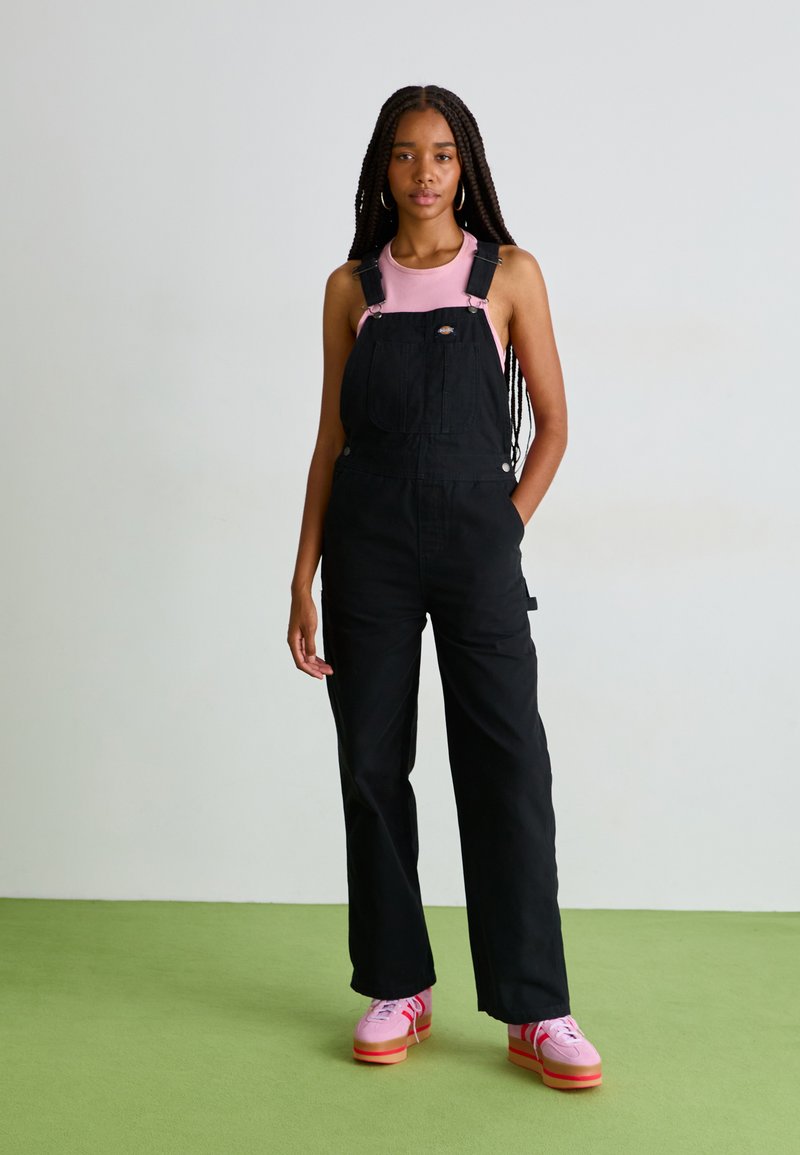 Črne denim naramnice s širokimi nogavicami in nastavljivimi naramnicami, oblečene čez roza top. Roza platforme s rdečimi in belimi podplati.