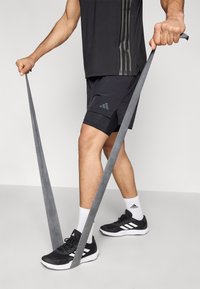 Μαύρο αθλητικό μπλουζάκι με τρεις κατακόρυφες ρίγες, μαύρο σορτς με πλαϊνή τσέπη, γκρι λάστιχο αντίστασης, μαύρα παπούτσια με λευκές λεπτομέρειες.