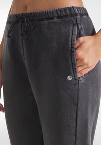 Schwarze Sweatpants mit einem elastischen Bund, Kordelzug, Seitentaschen und einem kleinen Logo an der linken Hüfte. Weicher Stoff.