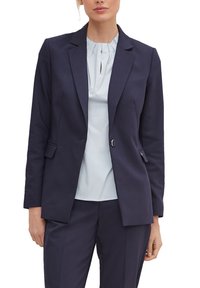 Blazer azul marino con un diseño ajustado, solapas de muesca, cierre de doble botón y dos bolsillos frontales. Combinado con una blusa de rayas azul claro.