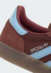 Baskets en daim marron avec accents en cuir bleu clair, présentant trois bandes bleues, une semelle extérieure en caoutchouc et le logo « SPEZIAL » sur le côté.