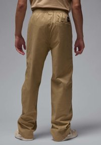 Khaki bukser med elastisk talje, løst fit og en enkelt baglomme. Stoffet har en glat tekstur med en subtil glans.
