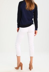 Granatowy sweter z fakturą i czarnymi rękawami, zestawiony z białymi spodniami o długości kostek i jasnobrązowymi szpilkami.