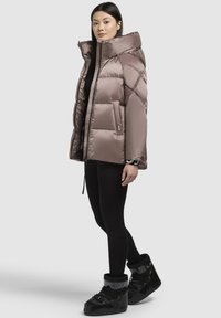 Padded, cropped jacket in taupe with a high collar, featuring diagonal stitching and two side pockets, paired with black leggings and boots.