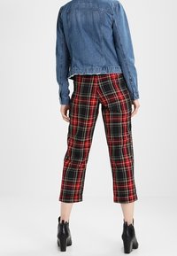 Jeansjacka med en kortad design, tillsammans med röd och svart rutig kortbyxor med gula och vita accenter. Svarta ankel boots.