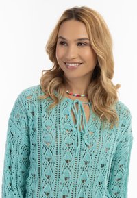 Pullover all'uncinetto azzurro chiaro con una vestibilità ampia, caratterizzato da uno scollo con lacci e da un intricato motivo in pizzo aperto. Texture e dettagli di design sottili.