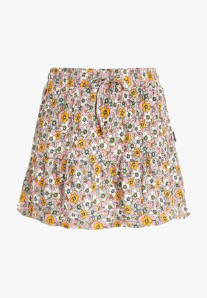 Gelbes Tanktop mit Palme-Grafik, kombiniert mit einem rosa, blümchenmusternden Rock mit Kordelzugbund. Getragen mit braunen Flip-Flop-Sandalen.
