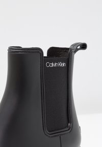 Bottines Chelsea noires Calvin Klein avec un dessus synthétique lisse, des panneaux élastiques sur les côtés et une languette au talon pour un enfilage facile.