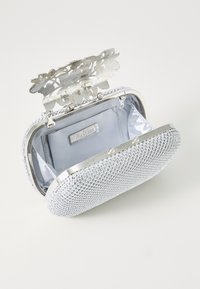Bolso de mano plateado con exterior de piedras brillantes, cierre en forma de flor y interior de satén. Tiene un bolsillo interior y una forma elegante y redondeada.