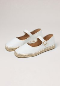 Baskets en toile blanches avec un orteil rond, une boucle sur le côté et une semelle en jute de style espadrille. Équipées d'un talon plat et d'une texture lisse.