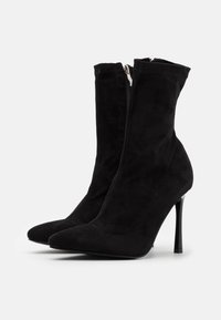 Bottines à talons hauts noires en daim doux, avec un bout pointu et une fermeture éclair sur le côté. Texture lisse avec un design épuré.