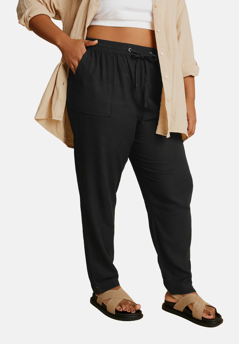 Czarne, luźne spodnie wykonane z lekkiego materiału, z elastycznym paskiem, sznurkiem i bocznymi kieszeniami, połączone z brązowymi sandałami na paski.