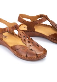 Sandali in pelle marrone con design intagliati, cuciture decorative e una cinturino regolabile alla caviglia per una vestibilità sicura.