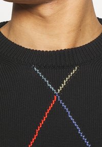 Černý pletený svetr s žebrovaným výstřihem, zdobený barevným vyšíváním v červené, modré, zelené a žluté, tvořícím vzor X přes hruď.