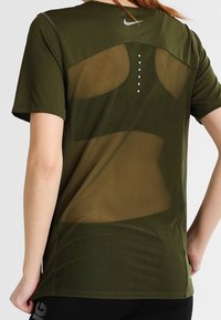 Oliwkowa koszulka sportowa Nike z siateczkowym tyłem, z pięcioma pionowymi otworami wentylacyjnymi, krótkimi rękawami i odblaskowym logo.