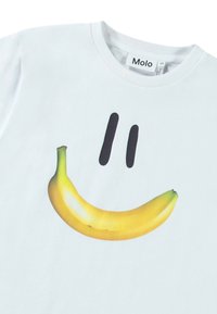Hvid bomulds T-shirt med et stort gult bananmotiv og to sorte buede linjer over, der ligner et smil. Etiketten er synlig ved halsen.