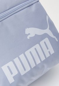 Lichtblauwe stoffen tas met een wit Puma-logo en grote letters. Glad textuur met een duurzame, ritssluiting.
