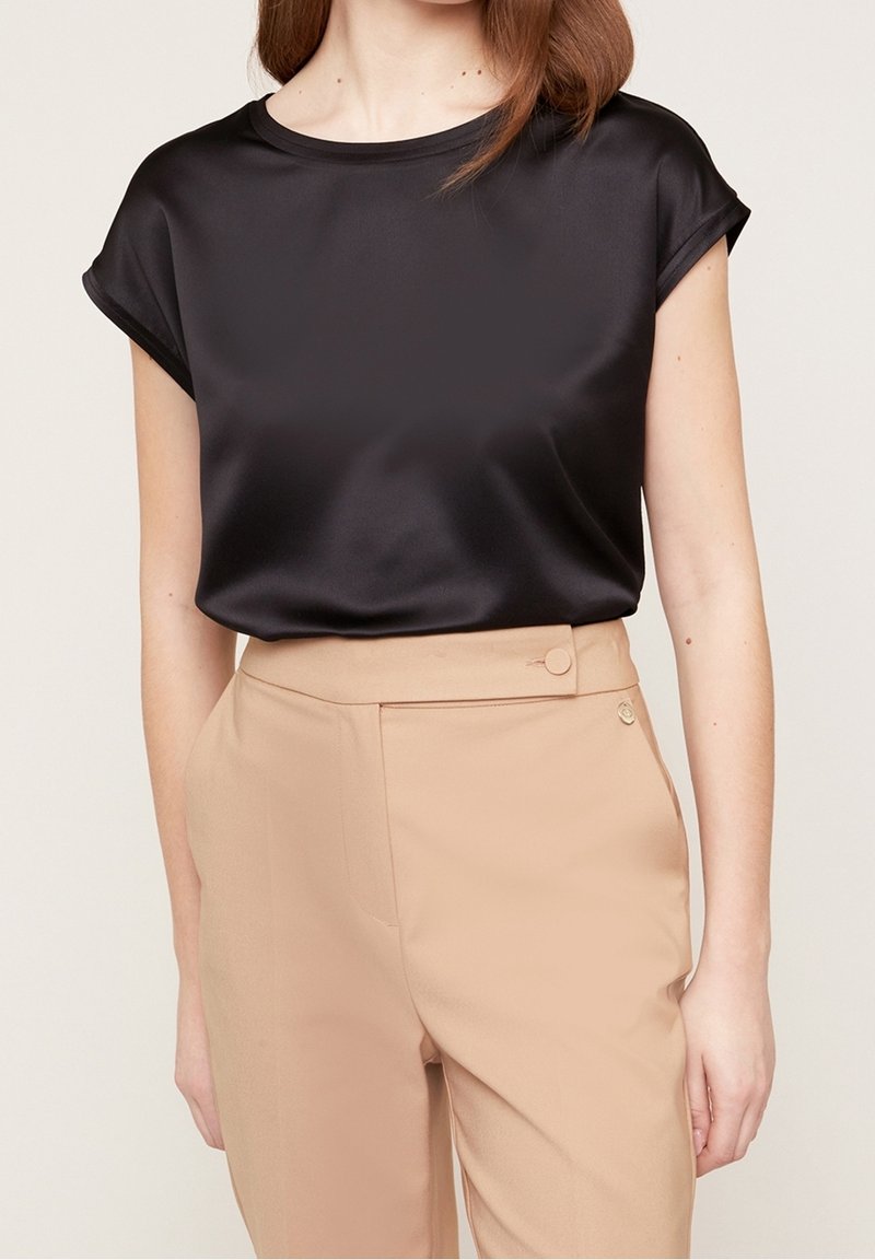 Svart satin topp med korta upprullade ärmar, kombinerad med smalt skurna beige byxor med sidoknapsdetalj och en mjuk textur.