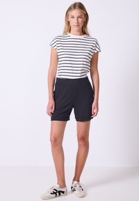 Pruhovaná košile s krátkými rukávy v bílé a černé barvě, spárovaná s černými šortkami. Černý pás, ohrnuté manžety a bílé tenisky s černými akcenty.