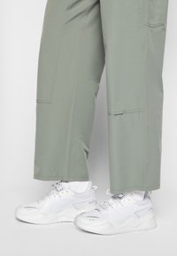 Vita atletiska sneakers med nät- och syntetpaneler, tillsammans med ljusgröna, löst sittande byxor med sidofickor och sydda detaljer.