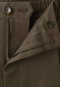 Nærbillede af brun stof, der viser en åben lynlås med to mørke knapper og matchende knaphuller på et par bukser.