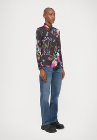 Camicia a maniche lunghe floreale nera, con colori vivaci e colletto. Abbinata a jeans blu in denim e scarpe nere.