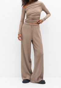 Haut côtelé à épaules dénudées beige, associé à un pantalon large assorti. Les deux présentent une texture douce, une taille à cordon de serrage et une coupe décontractée.