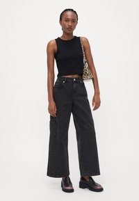 Top cropped preto, calças cargo largas em cinza escuro com bolso lateral, e sapatos pretos com um destaque em gradiente roxo. Mala com padrão de zebra.