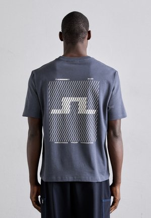 T-shirt en coton gris avec un design graphique au dos, comportant un motif géométrique blanc et un texte superposé, à manches courtes et col rond.