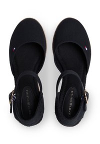 Μαύρα πάνινα παπούτσια με στρογγυλεμένη μύτη, ρυθμιζόμενο λουράκι και ανάγλυφο τακούνι. Διαθέτουν χρυσά μεταλλικά στοιχεία και μια μικρή λεπτομέρεια με λογότυπο.