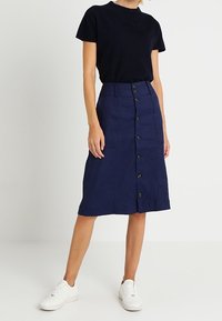 Navy button-up midi skirt with a slight A-line shape, made of woven fabric, paired with a dark T-shirt and white sneakers.