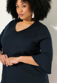 Mörkblå, v-ringad topp med trekvartslång ärm, tillverkad av mjukt tyg. Har utsvängda ärmslut och en avslappnad passform.