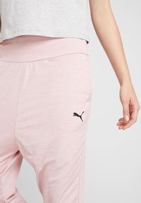 Lichtroze sportbroek met een brede tailleband, voorzien van een zwart Puma-logo op de linker dij en een gladde, zachte textuur.
