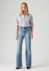 Chemise rayée à manches longues avec un col boutonné associée à un jean flare taille haute bleu clair. Des chaussures noires à talons complètent la tenue.